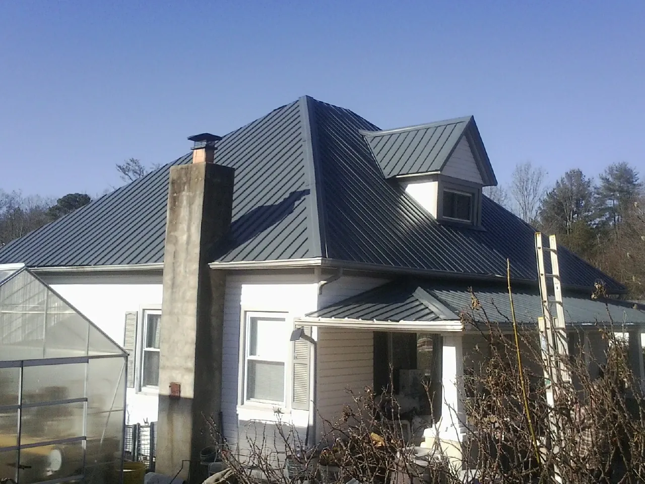Dark blue standing seam metal roof on a white farmhouse with dormer — Slate & Tile Roof Repair by Roofing Brothers in Ellicottville
