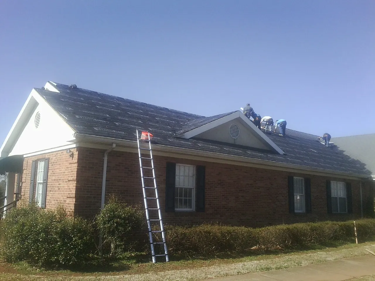 Crew tearing shingles off a brick ranch roof with a ladder set — Emergency Roof Repair work by our crew in Ellicottville