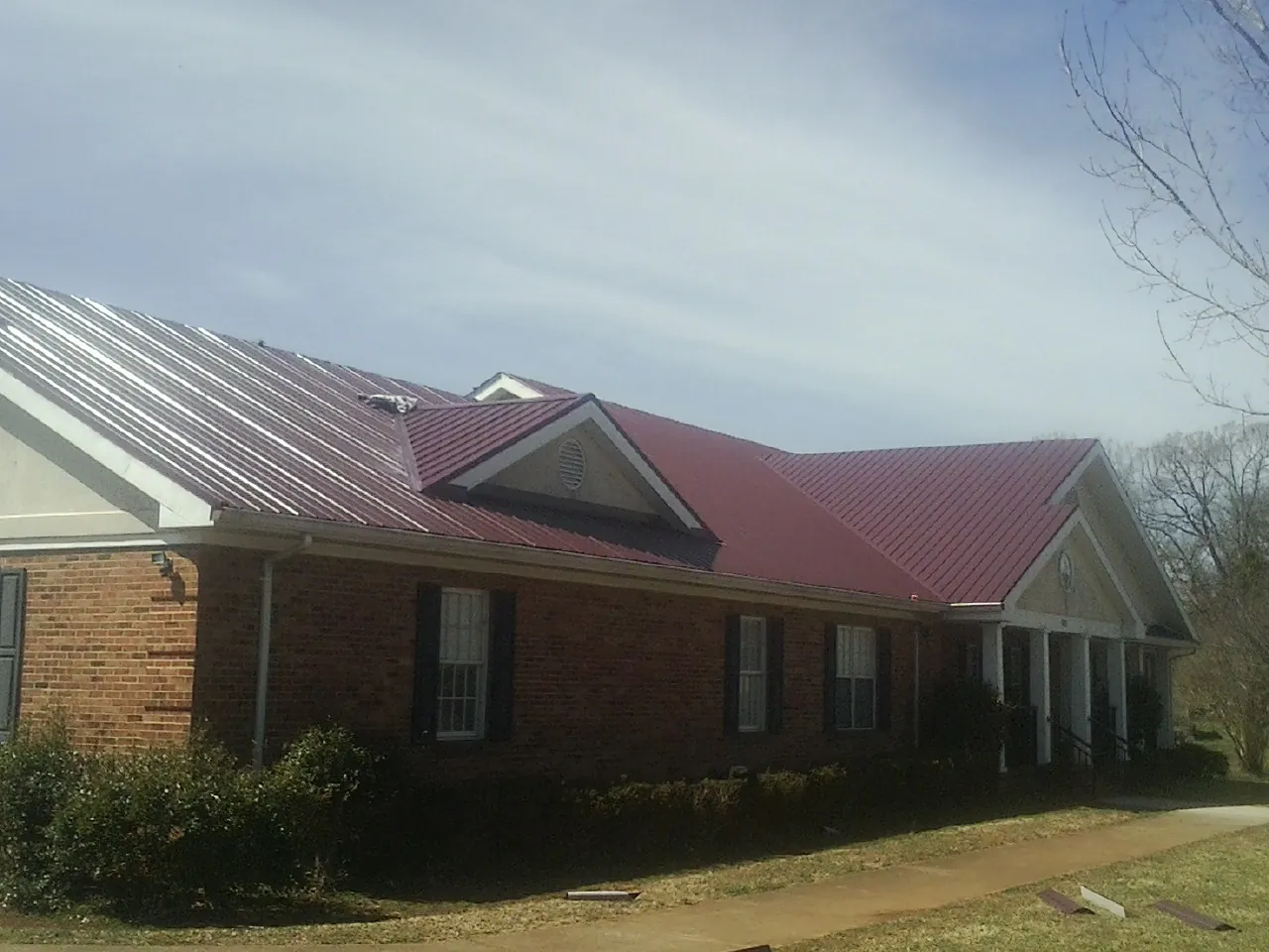 Red metal roof with gabled entries on a long brick building, from a Hail Damage Roof Repair job in Ellicottville