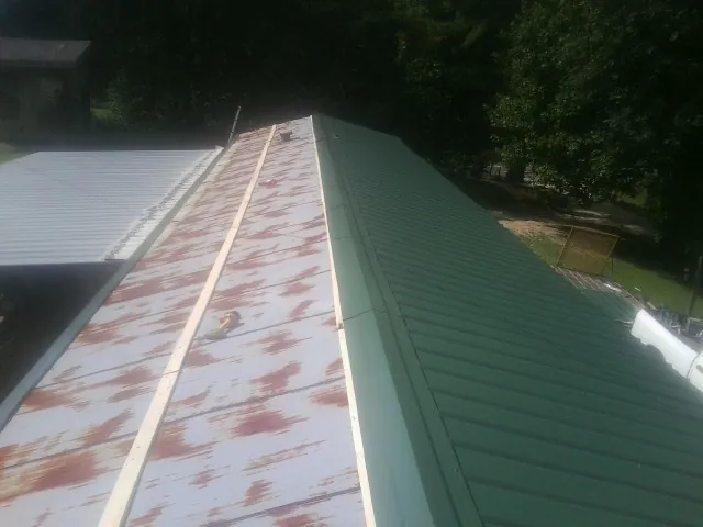 Old rusted panels beside newly installed green metal roofing — Wind Damage Roof Repair by Roofing Brothers in Ellicottville