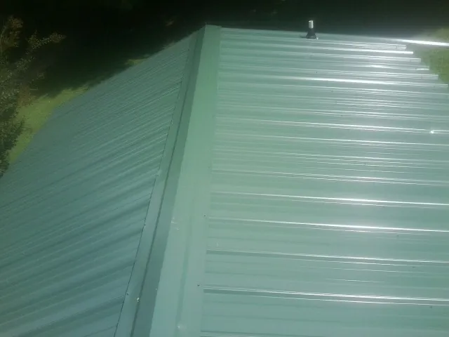 New green metal panels meeting at the ridge of a roof — Flat Roof Repair work by our crew in Ellicottville
