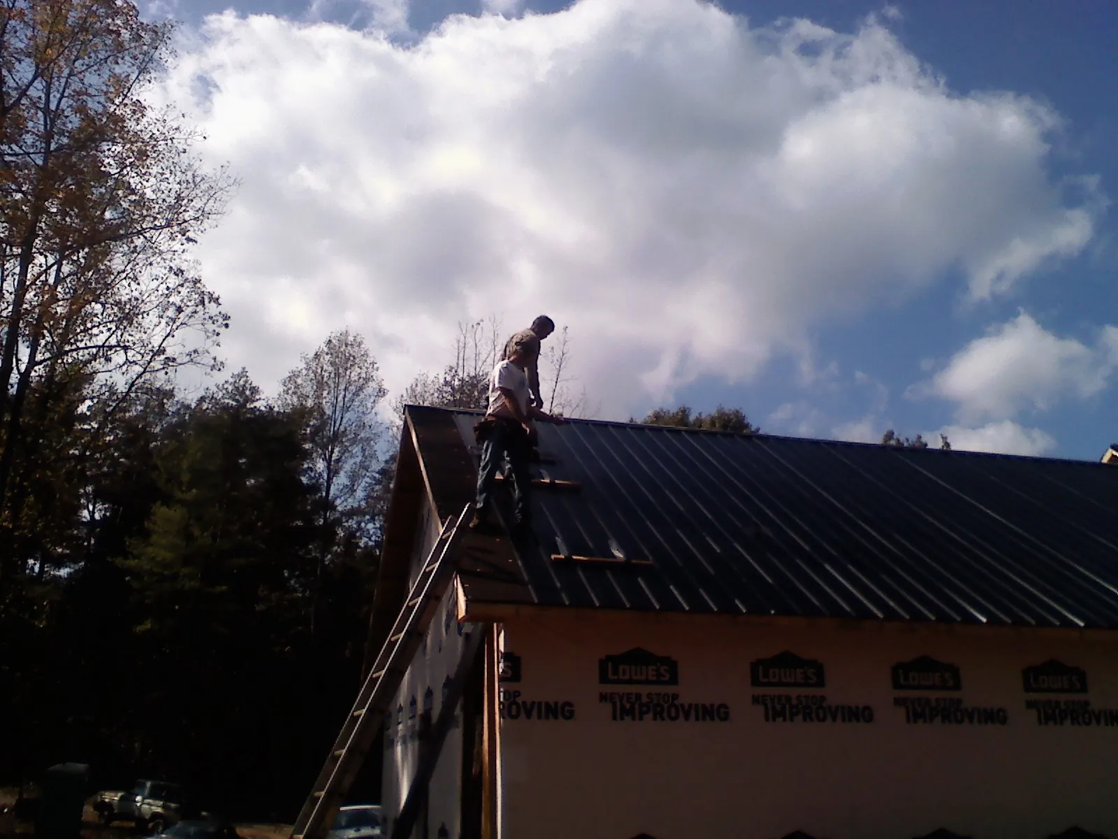 Roofer fastening dark metal panels high against a cloudy sky, from a Roof Inspection job in Ellicottville