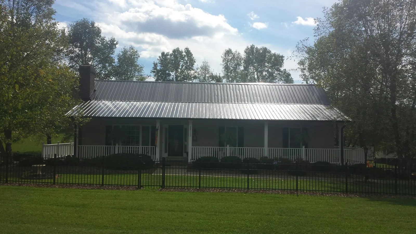 Gray metal roof on a brick ranch with a full width front porch — Gutter Guard Installation work by our crew in Ellicottville