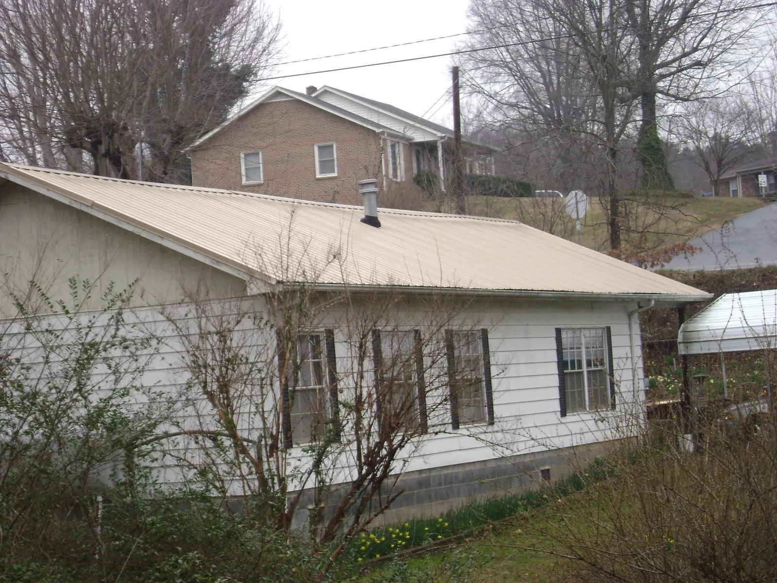 Tan metal roof on a white sided house set into a hillside — Commercial Roofing by Roofing Brothers in Ellicottville