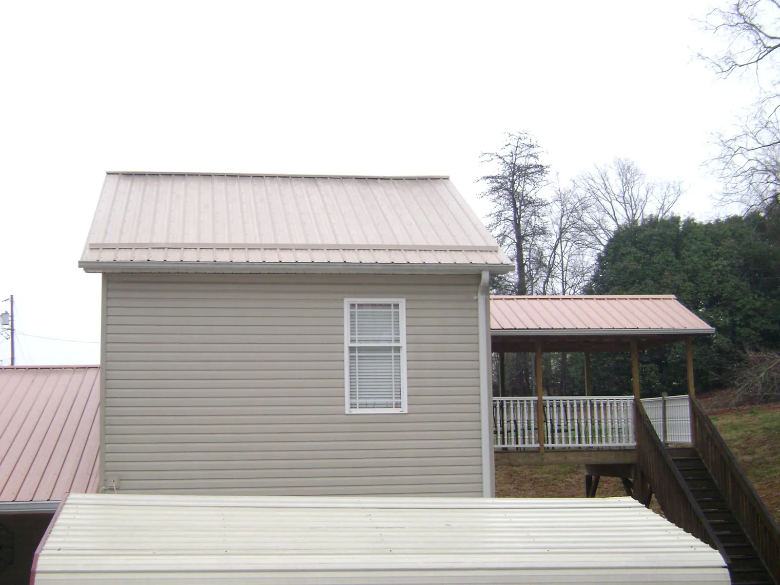 Tan metal roofs on a two story addition and attached porch, from a Roof Replacement job in Ellicottville